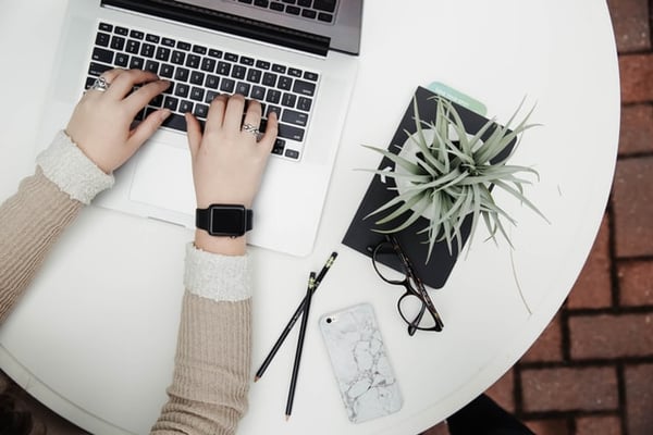 Person typing on a gray laptop next to a plant