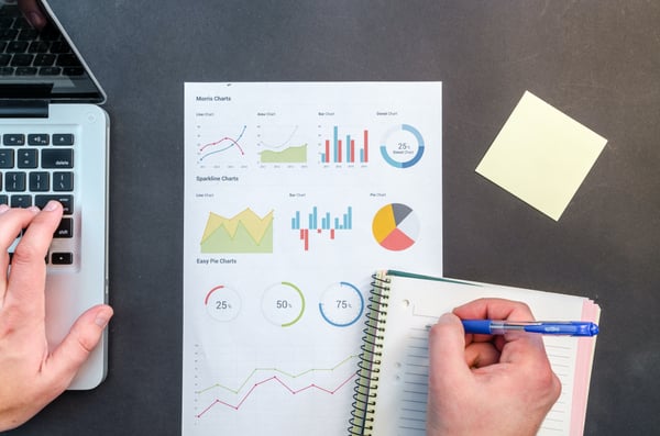 Person writing on notebook next to paper with graphs