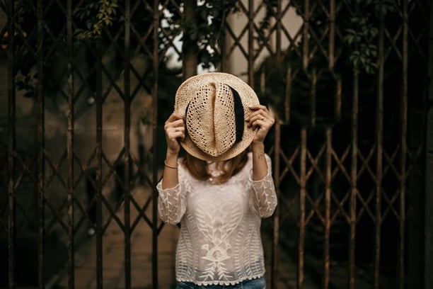 Woman keeping brown hat in front of her face